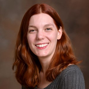 Smiling woman with shoulder-length red hair wearing a ribbed gray sweater