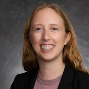 Smiling woman with blonde hair, wearing a black blazer with a lavender blouse