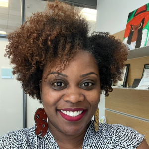 Smiling Black woman wearing a black and white patterned sleeveless blouse and statement earrings