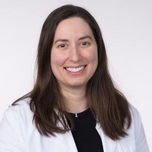 Smiling woman wearing a black blouse and a white medical lab coat