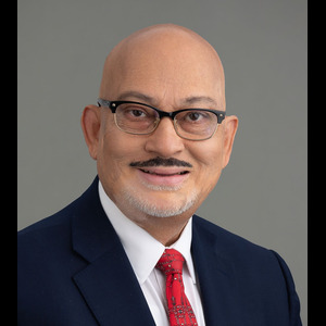 Smiling man wearing glasses, a blue blazer, red tie and white button up shirt