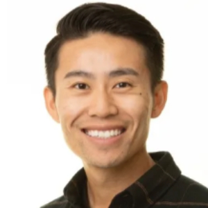 Asian man wearing black and brown plaid button-up shirt, smiling at the camera