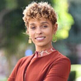 Smiling woman with blonde curly hair in an up-do, wearing a burnt orange blazer with a patterned collar