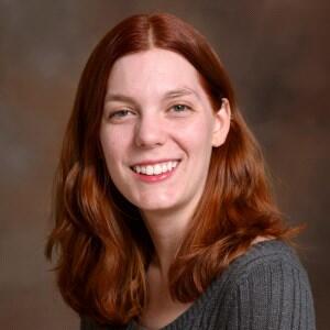 Smiling woman with shoulder-length red hair wearing a ribbed gray sweater