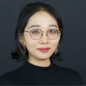 Smiling Asian woman wearing a black turtleneck, glasses, and gold statement earrings
