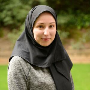 Smiling woman wearing a black hijab and gray long-sleeved shirt