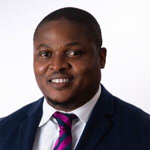 Smiling Black man wearing a blue blazer, white button up, and pink and blue tie